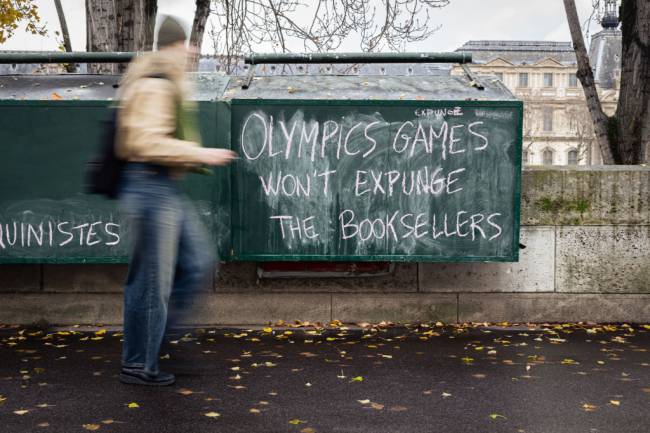 PARIS, FRANCE - 2023/12/13: A woman walks by a bookseller's stand with protest graffiti reading 