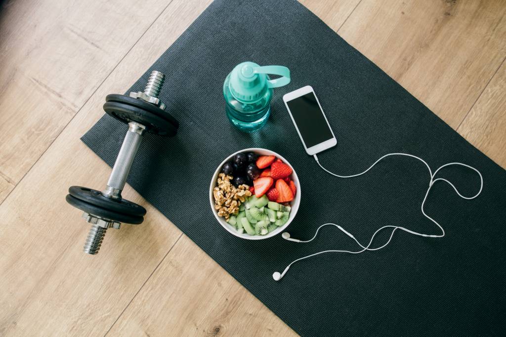 Dumbbell, drinking bottle, fruit bowl and smartphone with earphones COMBO EFICAZ - Prescrição: comida regrada e exercício não excluem prazer