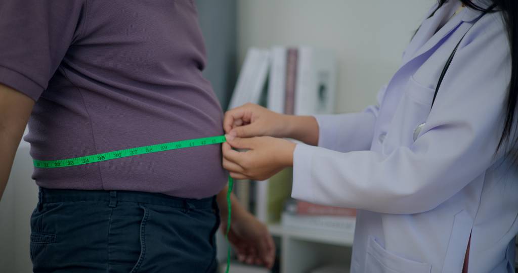 Female Nutritionist measuring waist of overweight man in weight loss clinic ALÉM DO IMC - Visão ampla: abordagem deve considerar outros critérios de saúde