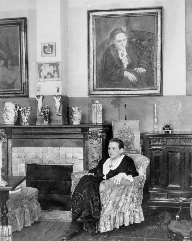 Gertrude Stein Relaxing in a Chair (Original Caption) Paris, France: Writer Gertrude Stein seated before a portrait of herself that was painted by Picasso.