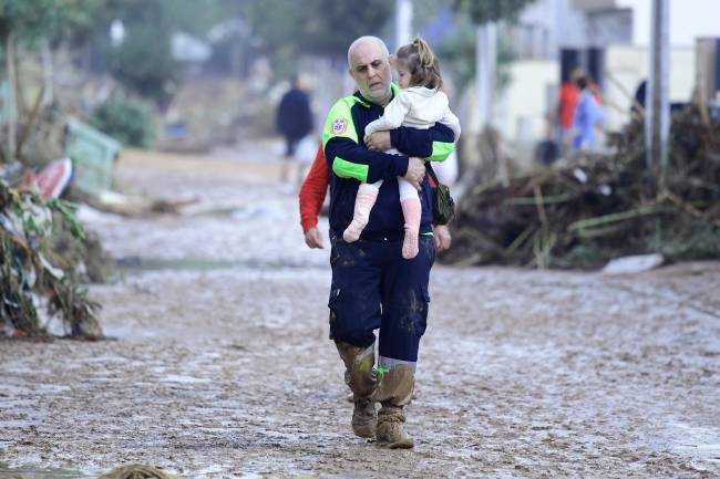SPAIN-FLOODS A Civil Protection member carries a child in a street covered in mud in a flooded area in Picanya, near Valencia, eastern Spain, on October 30, 2024. Floods triggered by torrential rains in Spain's eastern Valencia region has left 51 people dead, rescue services said on October 30. (Photo by Jose Jordan / AFP)