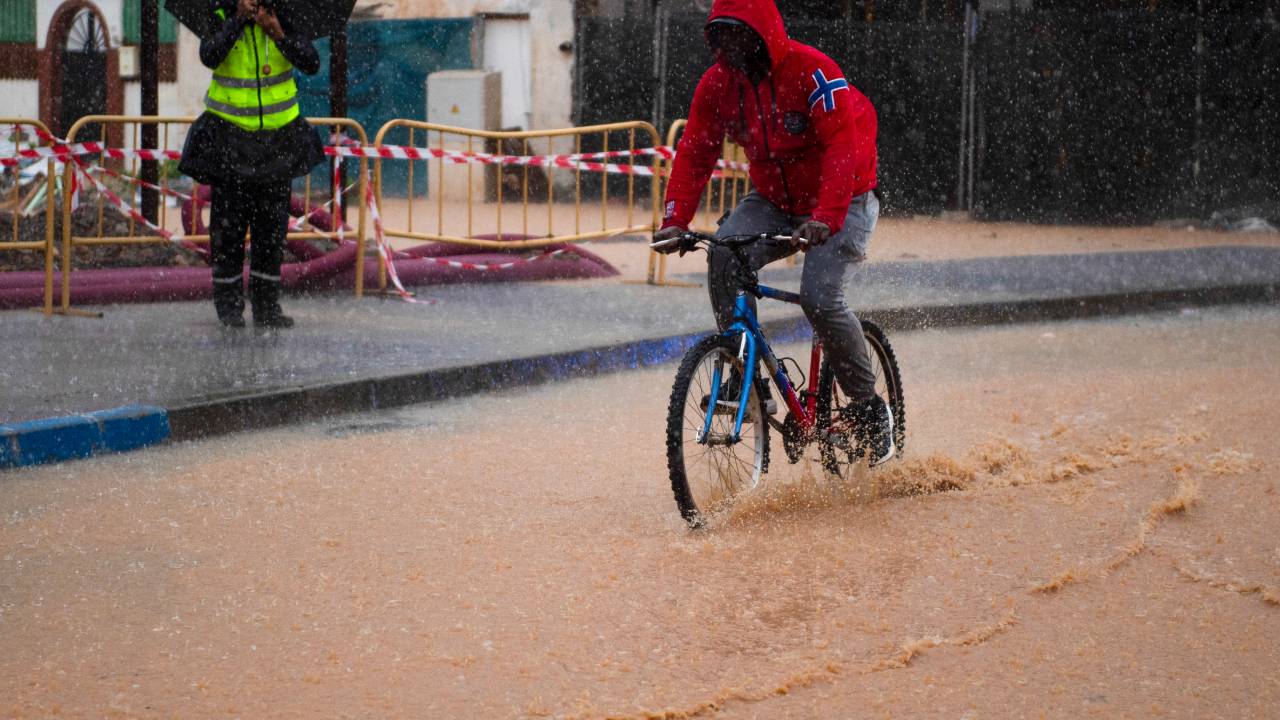 A man rides a bicycle down a flooded street in Campanillas, near Malaga, southern Spain, on November 13, 2024. Spain closed schools and evacuated residents as heavy rains lashed the country on November 13, two weeks after its worst floods in a generation killed more than 200 people. (Photo by JORGE GUERRERO / AFP)