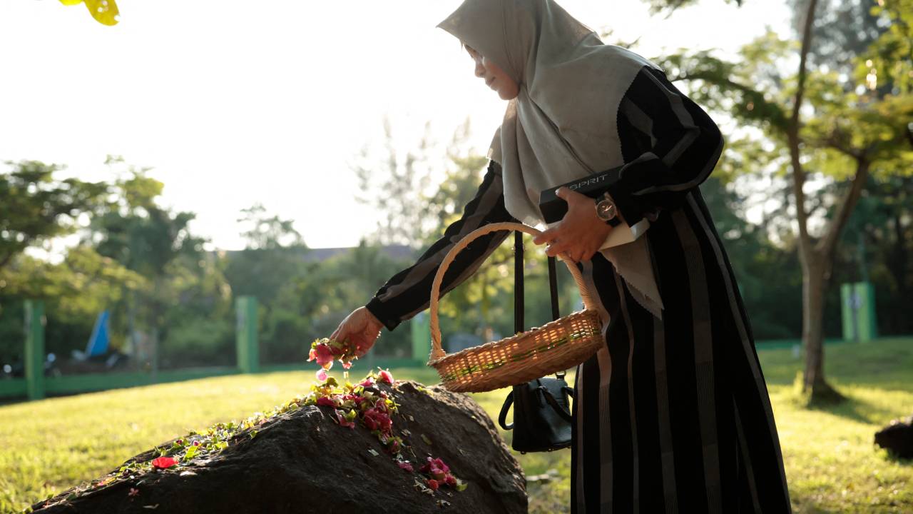 Mulher coloca pétalas de flores em vala comum na província de Aceh, na Indonésia, a mais atingida pelo tsunami do Oceano Índico em 2004. 26/12/2024