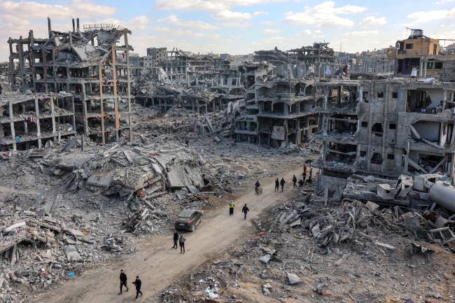 People walk past the rubble of damaged and collapsed buildings in Beit Lahia in the northern Gaza Strip on January 20, 2025 a day after a ceasefire deal in the war between Israel and Hamas went into effect. (Photo by Omar AL-QATTAA / AFP)