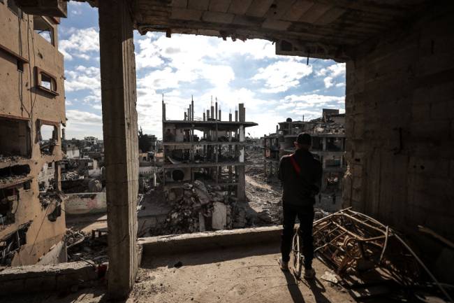 Palestinians continue to return to their homes as ceasefire comes into force in Gaza DEIR AL BALAH, GAZA - JANUARY 20: A man looks from inside a damaged building at the heavily damaged and partially collapsed buildings as displaced Palestinians continue to return their houses after the ceasefire and hostage-prisoner swap deal between Hamas and Israel at Bureij refugee camp in Deir al-Balah, Gaza on January 20, 2025. (Photo by Ali Jadallah/Anadolu via Getty Images)