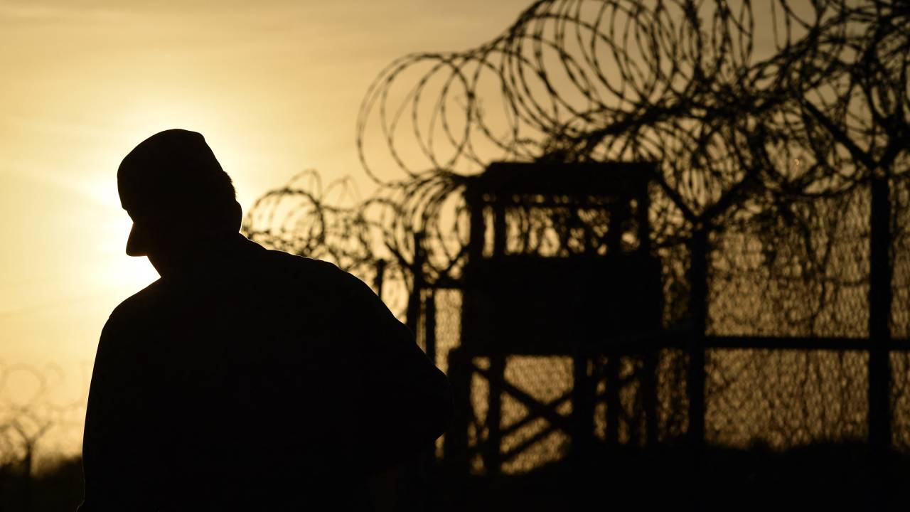(FILES) This photo made during an escorted visit and reviewed by the US military, shows an US soldier walking next to the razor wire-topped fence at the abandoned "Camp X-Ray" detention facility at the US Naval Station in Guantanamo Bay, Cuba, April 9, 2014. US President Donald Trump said on January 29, 2025, he planned to detain "criminal illegal aliens" at the notorious Guantanamo Bay military prison, used for holding terrorism suspects since the 9/11 attacks. Trump made the shock announcement as he signed a bill allowing the pre-trial detention of undocumented migrants charged with theft and violent crime -- named after a US student killed by a Venezuelan immigrant. (Photo by Mladen ANTONOV / AFP)