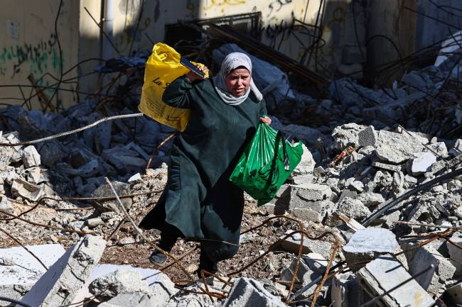 A woman carries bags as she walks on rubble at the Nur Shams camp for Palestinian refugees near Tulkarem, where Israeli forces allowed residents to retrieve belongings after issuing reported demolition notifications for several houses, amid a weeks-long offensive in the occupied West Bank on February 26, 2025. (Photo by Zain JAAFAR / AFP)