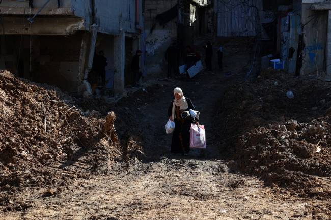 A woman carries belongings as she walks across a destroyed street while fleeing the Nur Shams camp for Palestinian refugees near Tulkarem, where Israeli forces allowed residents to retrieve belongings after issuing reported demolition notifications for several houses, amid a weeks-long offensive in the occupied West Bank on February 26, 2025. (Photo by Zain JAAFAR / AFP)