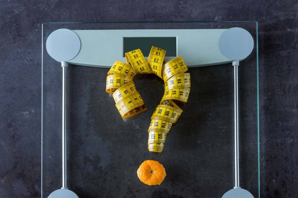 On the scales is measuring tape and fruit orange. Symbol-  question mark. Concept- lifestyle, sports and diet for weight loss.