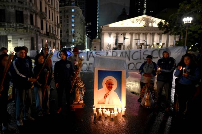 ARGENTINA-VATICAN-RELIGION-POPE Faithful Catholics light candles next to a picture of Pope Francis in front of the Cathedral in Buenos Aires on April 26, 2025, as his funeral takes place in Rome. The funeral for Pope Francis will be held on April 26, after the 88-year-old reformer died of a stroke on April 21, the Vatican announced. (Photo by Luis ROBAYO / AFP)