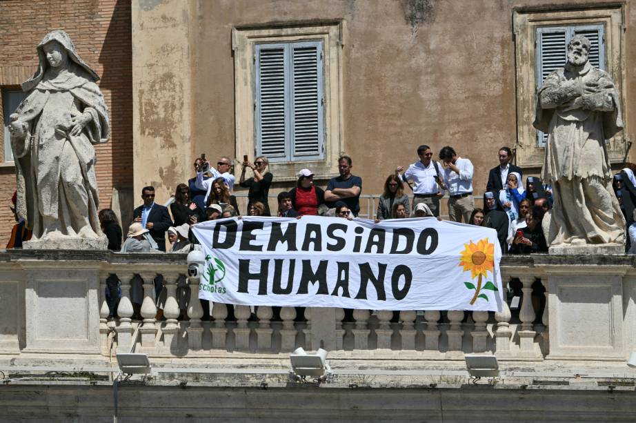 Pessoas seguram uma faixa com os dizeres 'Demasiado humano' enquanto participam da cerimônia fúnebre do falecido Papa Francisco. 26/04/2025 -