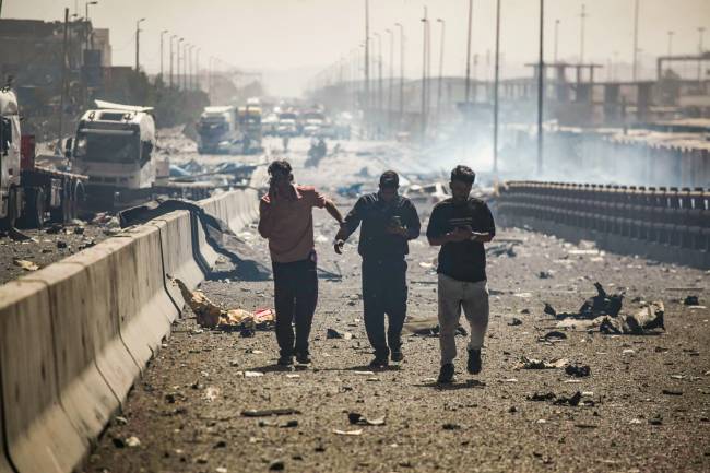 IRAN-PORT-EXPLOSION People use their telephones as they walk along a devastated boulevard following an explosion at the Shahid Rajaee port dock southwest of Bandar Abbas in the Iranian province of Hormozgan on April 26, 2025. Several containers exploded on April 26 at Iran's largest commercial port, authorities said, causing a major blast and fire, and leaving hundreds injured. Shahid Rajaee, more than 1,000 kilometres (620 miles) south of the capital, is the most advanced container port in Iran, according to the official IRNA news agency. (Photo by MOHAMMAD RASOLE MORADI / IRNA / AFP)