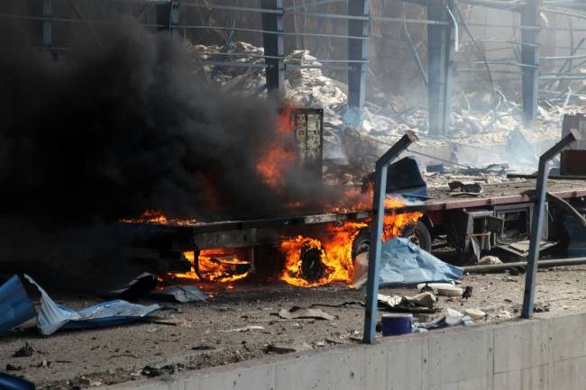IRAN-PORT-EXPLOSION Flames engulf a truck along a devastated boulevard following an explosion at the Shahid Rajaee port dock southwest of Bandar Abbas in the Iranian province of Hormozgan on April 26, 2025. Several containers exploded on April 26 at Iran's largest commercial port, authorities said, causing a major blast and fire, and leaving hundreds injured. Shahid Rajaee, more than 1,000 kilometres (620 miles) south of the capital, is the most advanced container port in Iran, according to the official IRNA news agency. (Photo by MOHAMMAD RASOLE MORADI / IRNA / AFP)