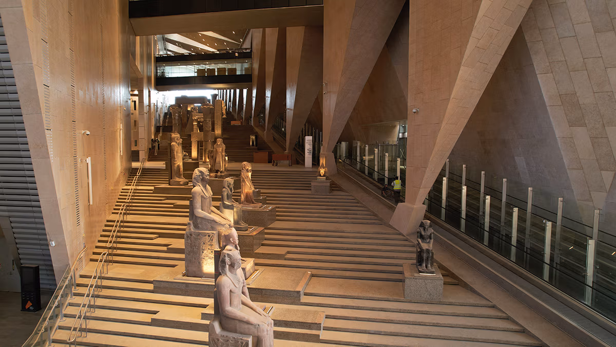 Escadaria monumental do Grand Egyptian Museum, ladeada por estátuas de faraós e deuses do antigo Egito, leva ao mirante com vista para as pirâmides.