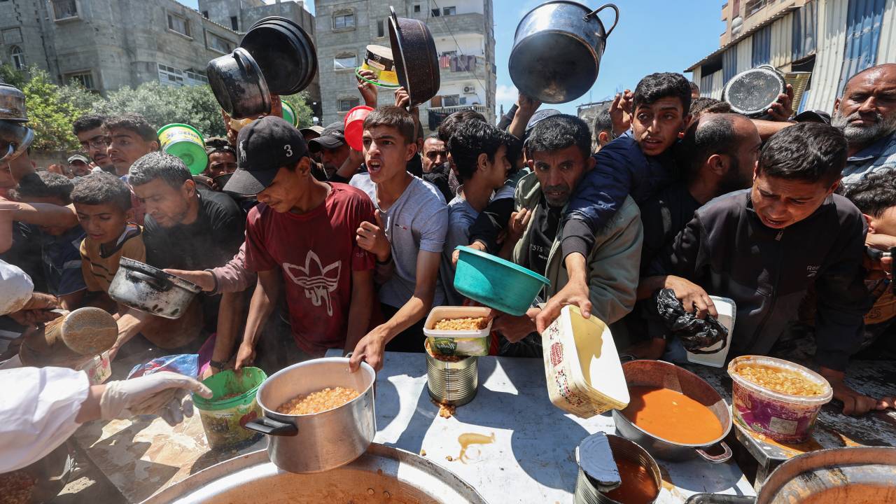Palestinians queue for a portion of hot food distributed by a charity kitchen at the Nuseirat refugee camp in the central Gaza Strip on May 5, 2025. The humanitarian crisis in the besieged Gaza Strip has worsened significantly since Israel blocked all aid from entering the territory on March 2, days before resuming its military campaign following the collapse of a ceasefire. (Photo by Eyad BABA / AFP)