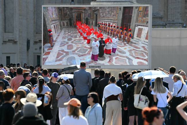 Faithful watch giant screen displaying images of the procession of cardinals to the Sistine chapel as the conclave to elect a new Pope starts, at St Peter's Square in The Vatican, on May 7, 2025. (Photo by Andreas SOLARO / AFP)