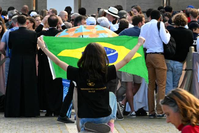A woman waves a Brazilian flag as faithful wait at St Peter's Square for smoke to rise from the chimney of the Sistine Chapel signalling the result of a conclave vote, in The Vatican, on May 7, 2025. (Photo by Andreas SOLARO / AFP)