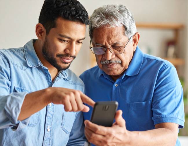 Idoso recebendo orientação de um familiar mais jovem contra golpes fraudes digitais Não deixe de orientar idosos e pessoas menos íntimas com tecnologia: alguém pediu dinheiro? Telefone para confirmar