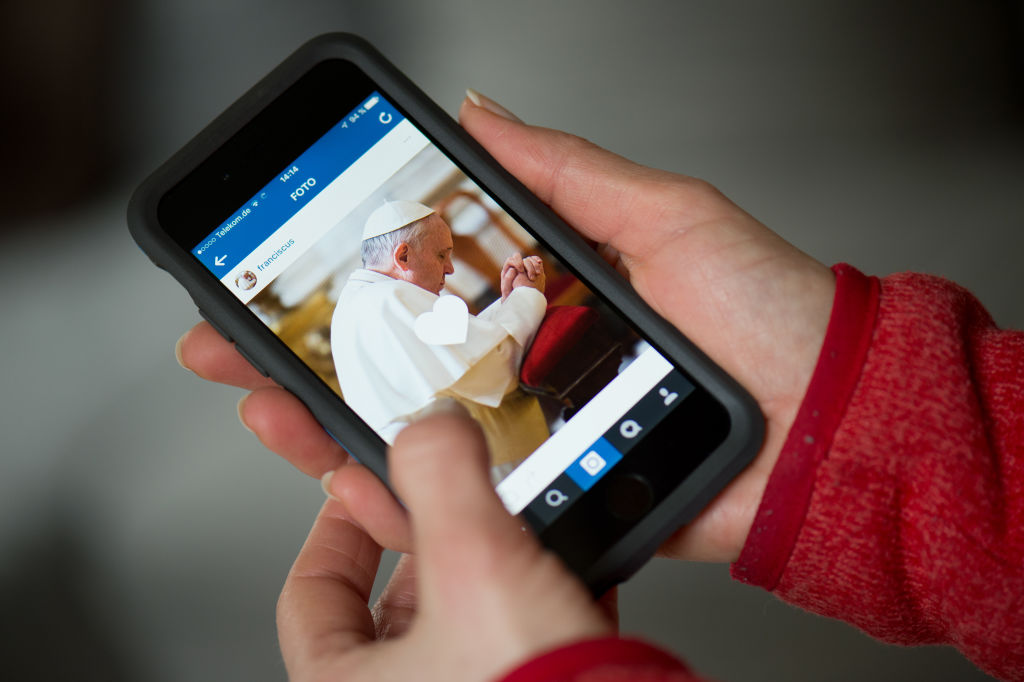 ILLUSTRATION - A woman holding a smartphone that shows the Instagram account of Pope Francis, Dresden, Germany, 19 March 2016. The pope starts sharing pictures and short videos with users all over the world using the account name 'Franciscus', the latin version of his name. PHOTO: ARNO BURGI/dpa | usage worldwide (Photo by Arno Burgi/picture alliance via Getty Images)