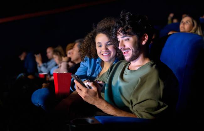 Casal jovem usa celular durante sessão de cinema Casal jovem usa celular durante sessão de cinema