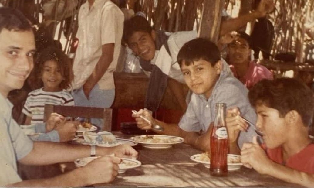 Robert Prevost à mesa com crianças no Peru, onde se vê um refrigerante típico. -