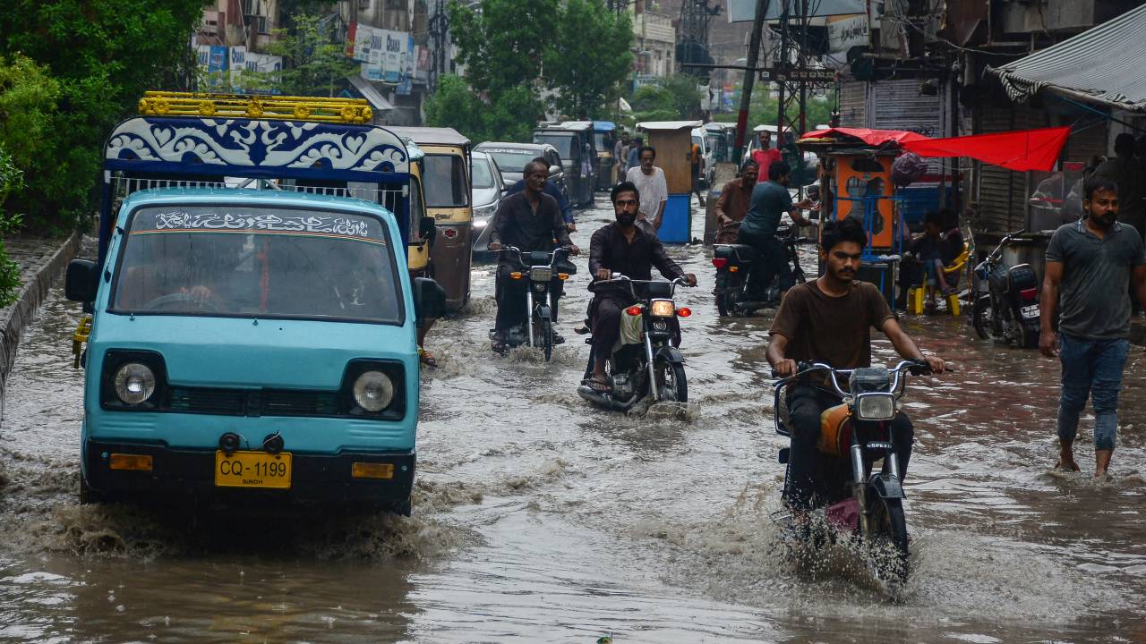 Passageiros atravessam uma rua inundada após fortes chuvas em Hyderabad, na província de Sindh, no Paquistão. 27/06/2025
