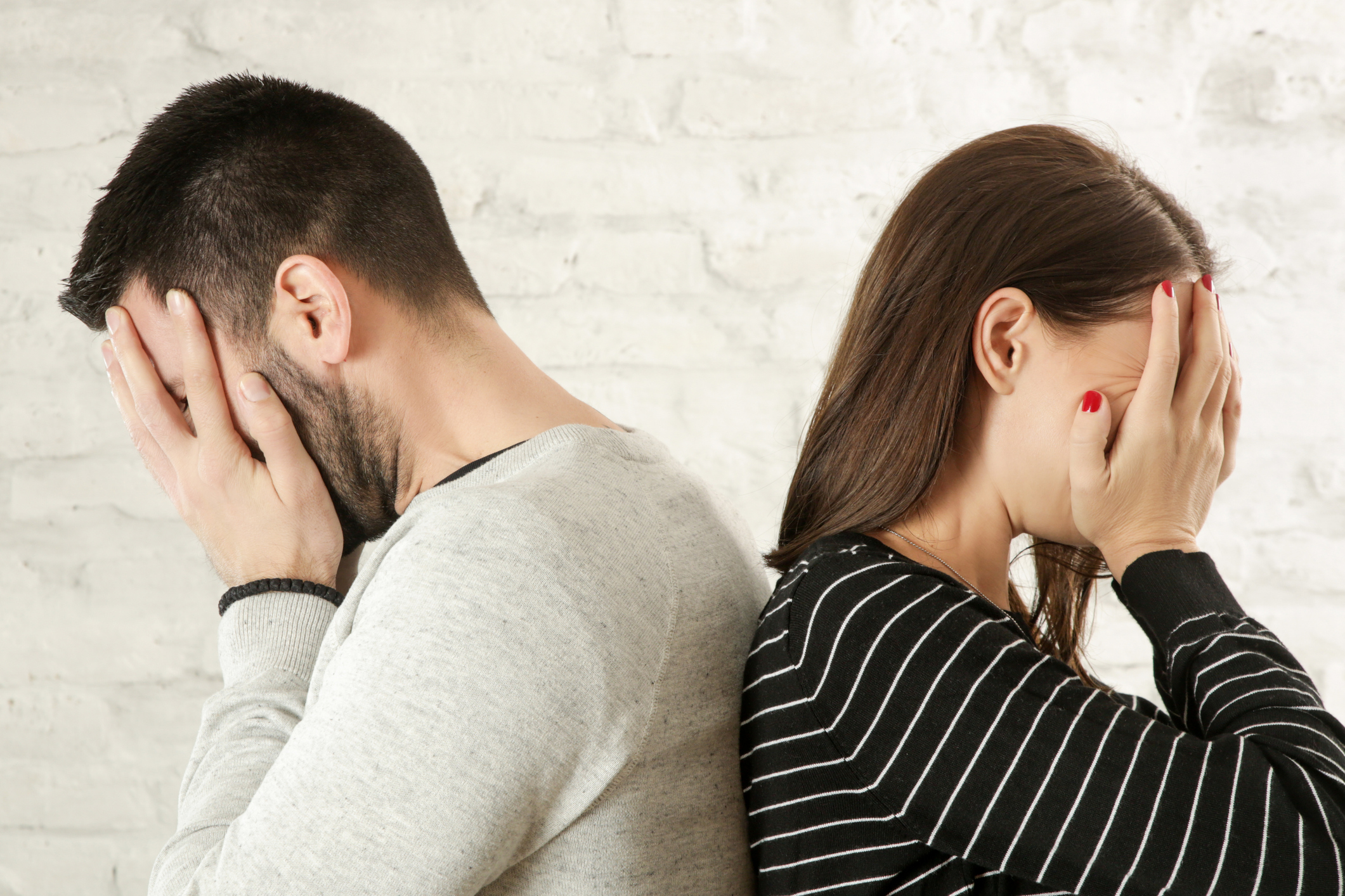 Side profile of a young couple standing back to back, hiding faces with hands