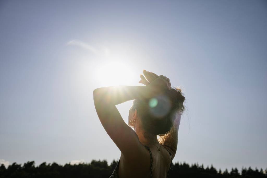 Sunlight shines into the camera while a woman  looks up at the sky