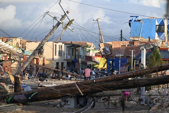 Electrical poles are down as a man bikes through the destroyed neighborood of North Street following the passage of Hurricane Melissa, in Black River, Jamaica on October 29, 2025. Hurricane Melissa bore down on the Bahamas October 29 after cutting a path of destruction through the Caribbean, leaving 30 people dead or missing in Haiti and parts of Jamaica and Cuba in ruins. Somewhat weakened but still threatening, Melissa will bring damaging winds and flooding rains to the Bahamas Wednesday before moving on to Bermuda late Thursday, according to the US National Hurricane Center (NHC). (Photo by Ricardo MAKYN / AFP)