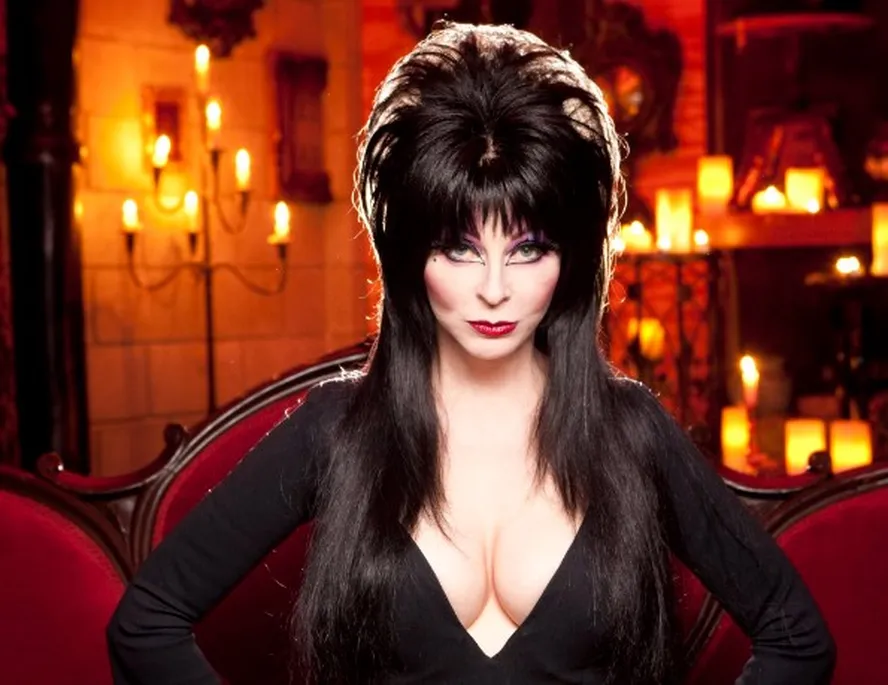 Foto da atriz Cassandra Peterson caracterizada como Elvira, com trajes pretos e maquiagem marcada
