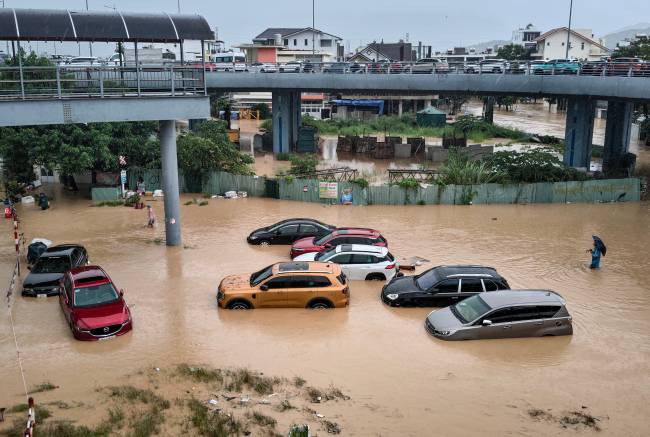 A man (R) wades through floodwaters near inundated vehicles in Nha Trang, Vietnam's coastal province of Khanh Hoa on November 20, 2025. Rescuers plucked stranded people from the rooftops of submerged homes as widespread flooding inundated central Vietnam, where authorities said on Thursday at least 16 people were killed. (Photo by Duc Thao / AFP)