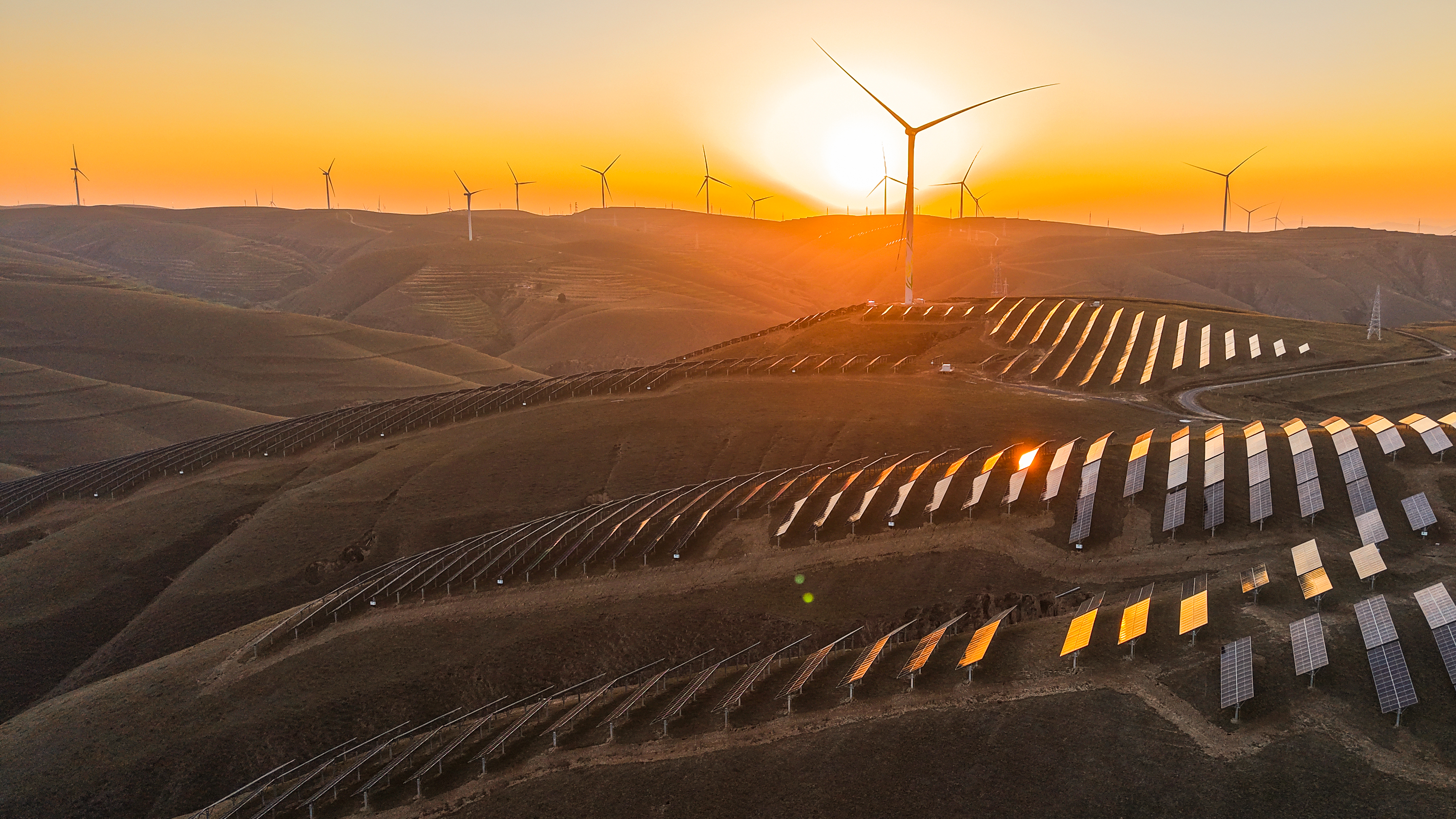 Em uma vista aérea, o brilho do pôr do sol ilumina turbinas eólicas e fileiras de painéis solares em um parque de energia eólica em 28 de outubro de 2025, em Qingyang, na província de Gansu, China