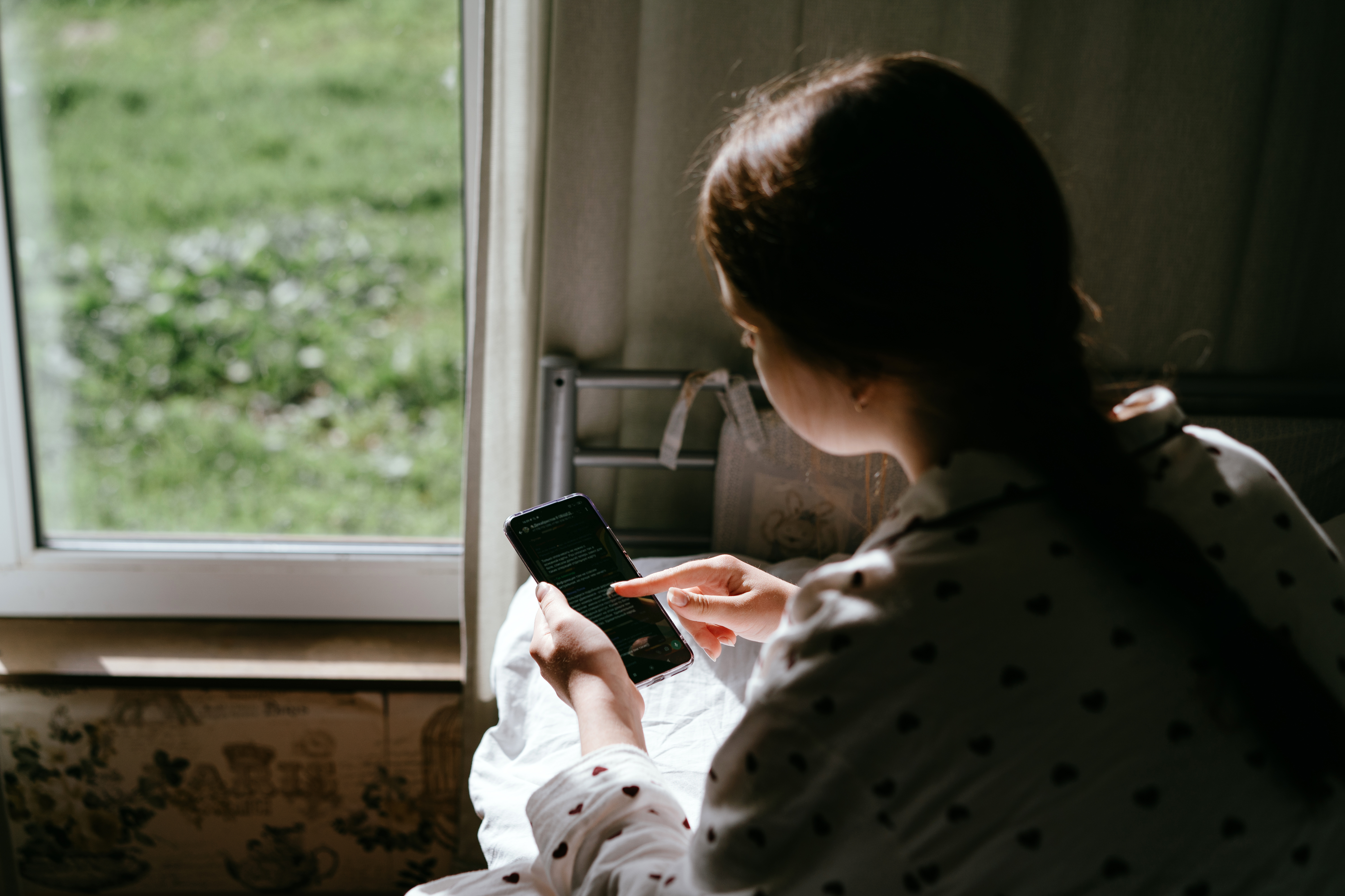 Portrait of a teenage girl with mobile phone sitting by the window in the village house. Concept of depression, loneliness, problems of adolescence