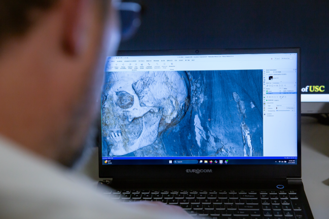 Foto de cientista usando computador com tomografia computadorizada de m&uacute;mia na tela.