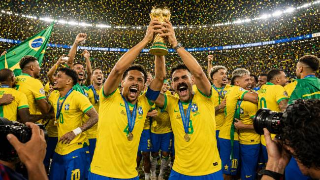 Jogadores da sele&ccedil;&atilde;o brasileira de futebol, em camisas amarelas, celebram com a ta&ccedil;a dourada da Copa do Mundo erguida por dois deles, enquanto confetes dourados caem sobre o campo. Um jogador com barba e bigode escuros grita de alegria, e outro, &agrave; esquerda, tamb&eacute;m sorri. Ao fundo, uma bandeira do Brasil &eacute; vis&iacute;vel, e outros atletas comemoram.