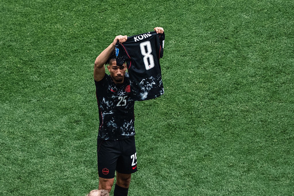Jogador de futebol com barba, vestindo uniforme preto com detalhes brancos e n&uacute;mero 25, ergue uma camisa preta com o nome KOBE e o n&uacute;mero 8 em branco, em um campo de grama verde