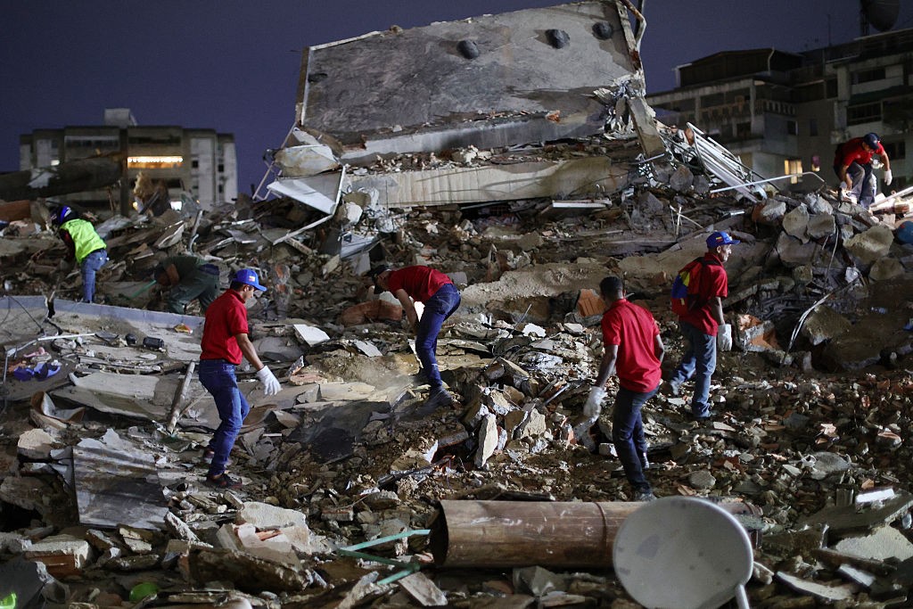 Equipe de resgate em meio a escombros de um prédio desabado à noite, com alguns usando capacetes e luvas, procurando por sobreviventes ou vítimas CARACAS, VENEZUELA - JUNE 24: Responders search for victims in a demolished building at San Bernardino after a magnitude 7.2 earthquake struck Venezuela and other regions in the Caribbean on June 24, 2026 in Caracas, Venezuela. According to the U.S. Geological Survey (USGS), the main earthquake was followed by a 7.5-magnitude aftershock less than a minute later; although some buildings collapsed, the number of victims remains unknown. (Photo by Jesus Vargas/Getty Images)