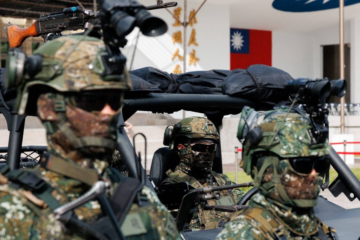 Três soldados taiwaneses em uniformes camuflados e capacetes, com óculos escuros e balaclavas, estão em um veículo militar. Um deles está ao volante, e a bandeira de Taiwan é visível ao fundo