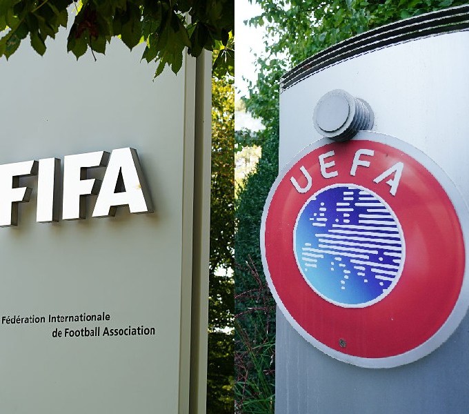 Placas com os logotipos da FIFA e da UEFA. À esquerda, a placa cinza da FIFA tem letras prateadas e o texto Fédération Internationale de Football Association. À direita, a placa da UEFA exibe o logo circular vermelho com o mapa-múndi azul e branco
