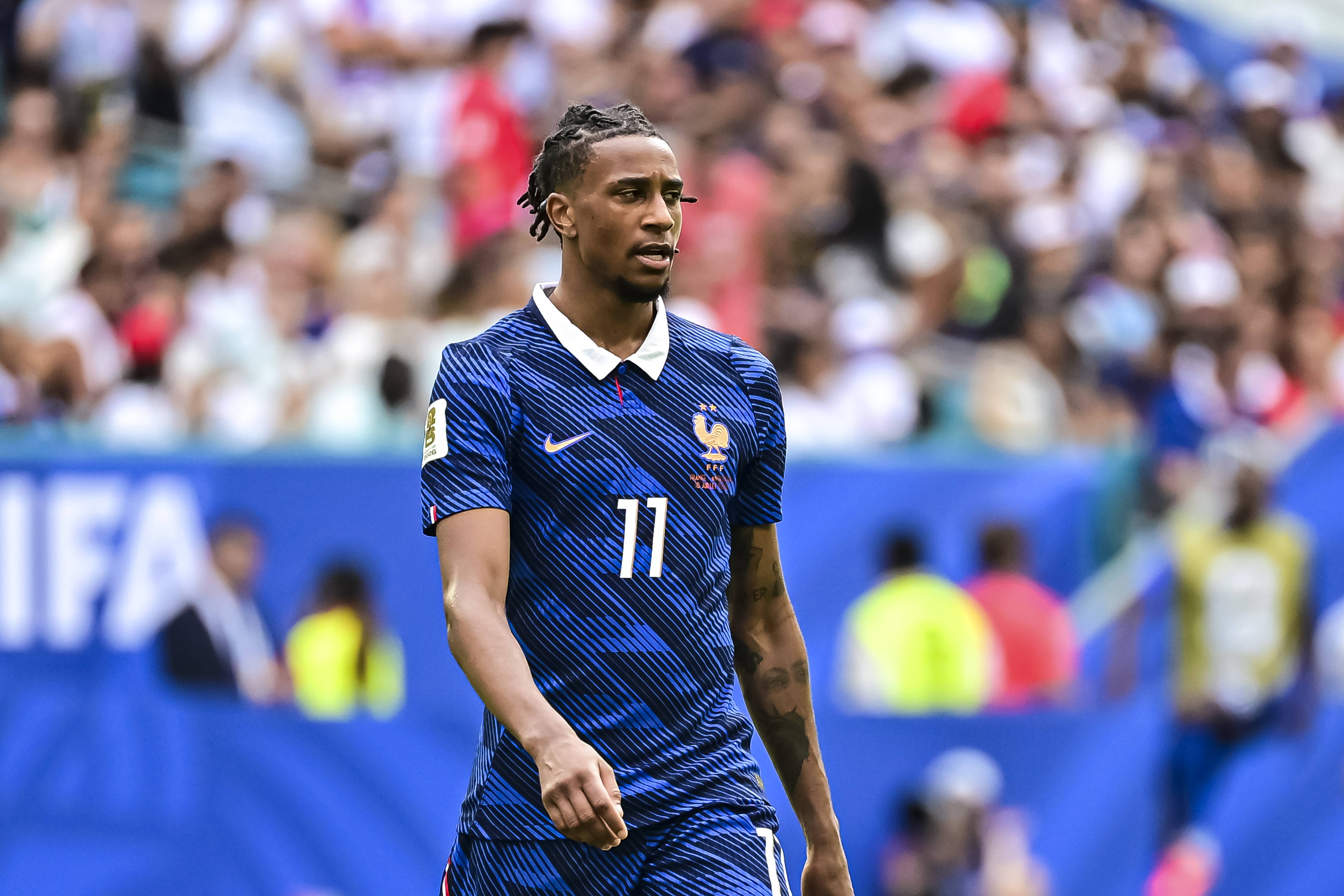 Jogador de futebol com dreads, camisa azul da França número 11 e gola branca, em campo com torcida ao fundo