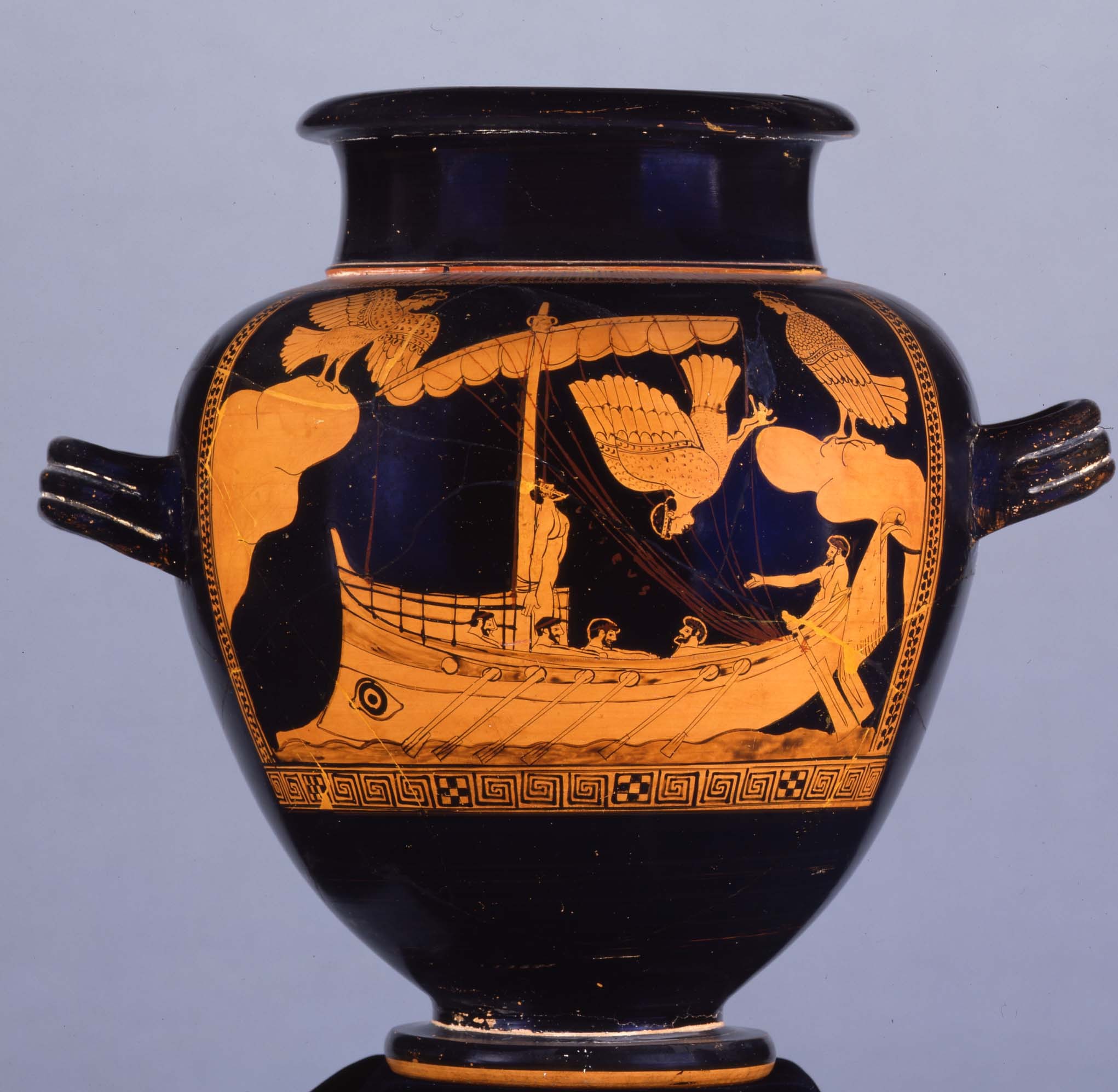 Vaso grego antigo com pintura em laranja e preto. A cena retrata um navio com remadores e um homem amarrado ao mastro, enquanto duas sereias aladas voam sobre a embarca&ccedil;&atilde;o, e um homem em terra gesticula.