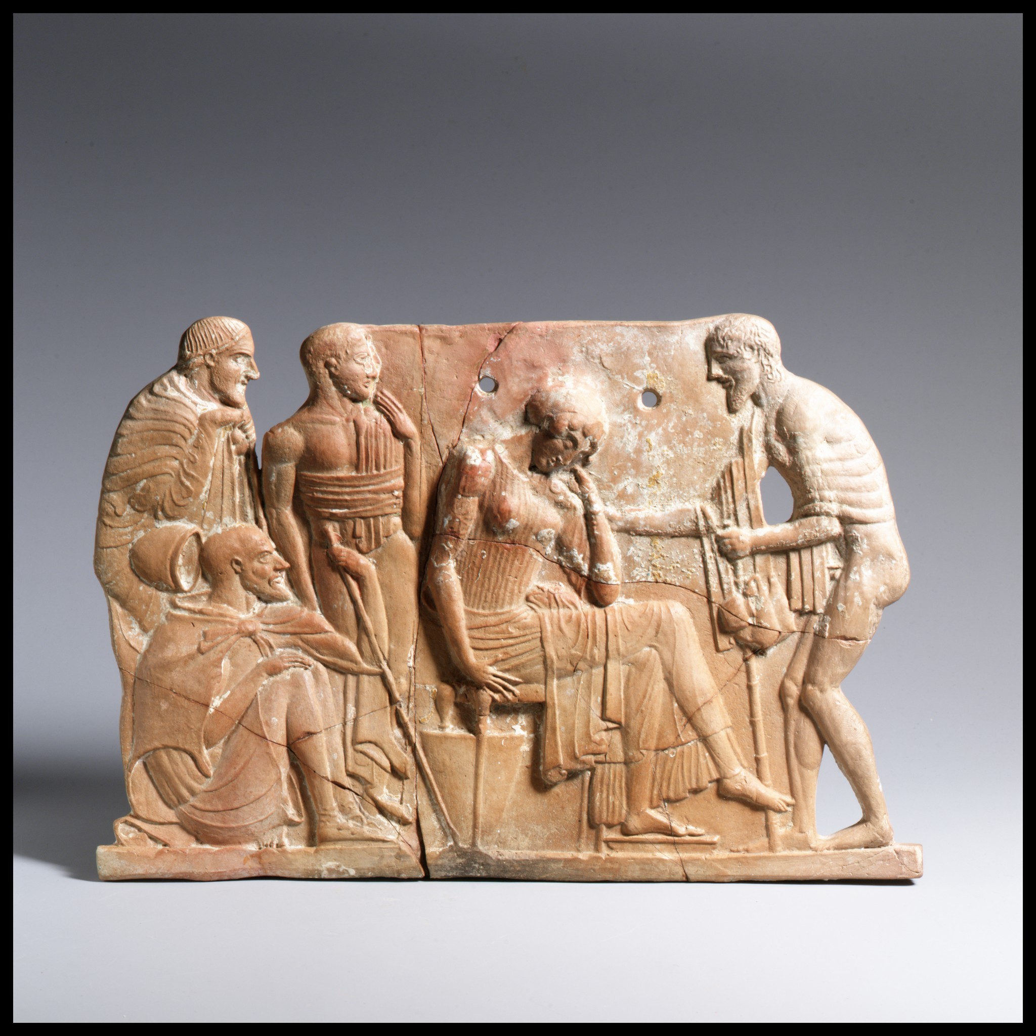 Relevo de terracota antigo com seis figuras. Uma mulher sentada, com a m&atilde;o no rosto, parece aflita. Um homem toca lira ao lado dela. Outros quatro homens observam, um deles agachado. A pe&ccedil;a tem rachaduras e furos, indicando desgaste pelo tempo
